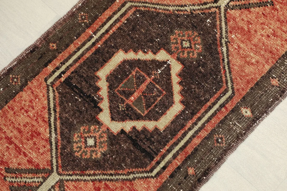 Close-up detail of the central brown medallion with beige and olive geometric patterns on the rust field.