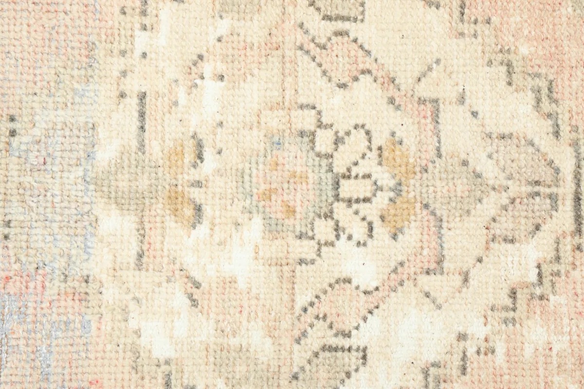 Close-up detail of the central medallion and surrounding geometric patterns in the beige and rose rug.