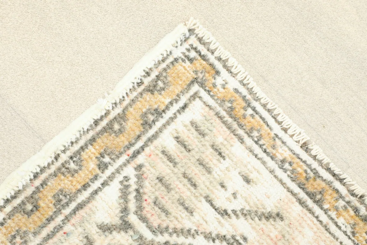 Detail of a corner of the rug, showing the gold and gray patterned border and fringe.