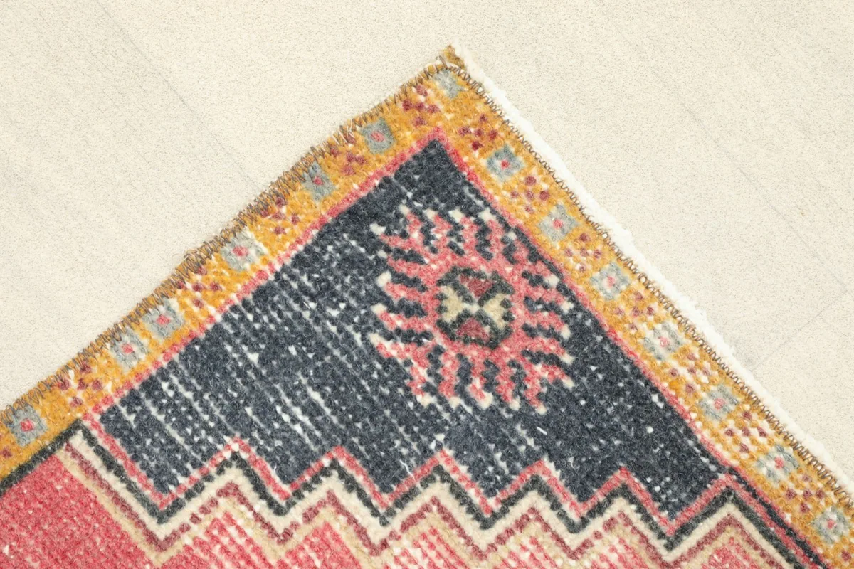 Corner detail showing the navy border with a rose stylized floral motif and the outer orange trim.