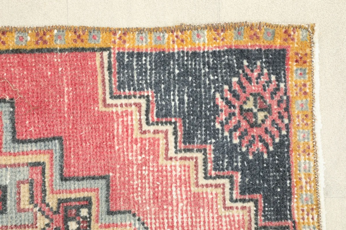 Side view of the rug's navy border and the stepped edge of the rose field, highlighting the vintage patina.