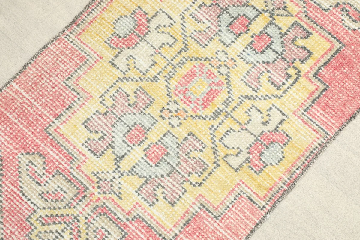 Angled close-up view of the rug's surface, highlighting the vibrant rose and yellow colors and geometric design.