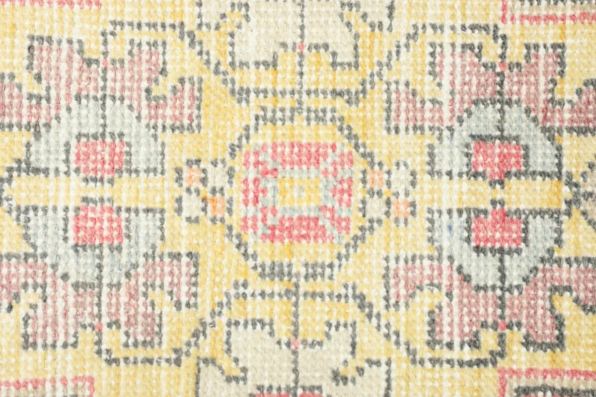 Detailed overhead view of the central geometric medallion and surrounding motifs in yellow, rose, and gray.