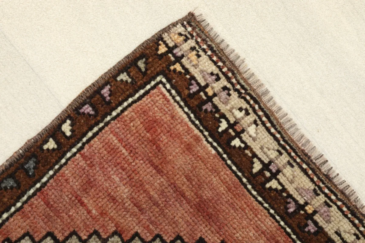 Corner detail of the rug, showing the rich brown border with small geometric accents and the red field.