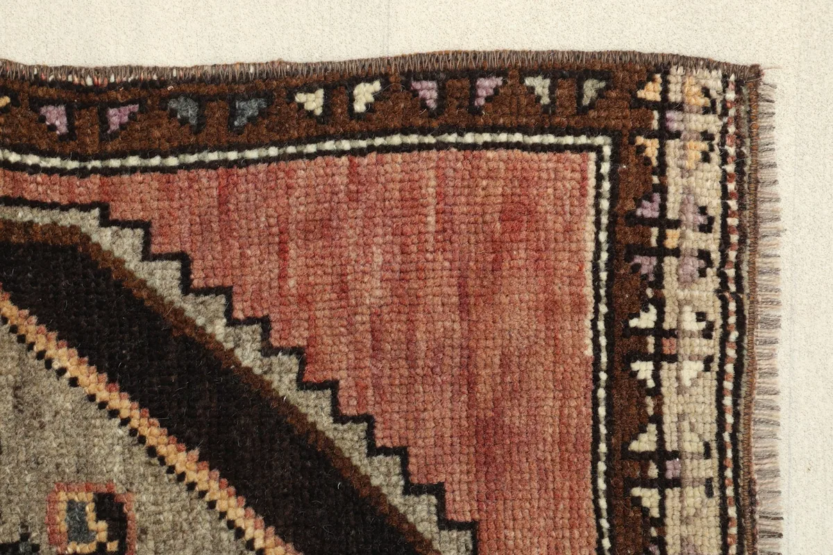 Edge detail of the rug, illustrating the distinct brown border, the red field, and the gray inner pattern.