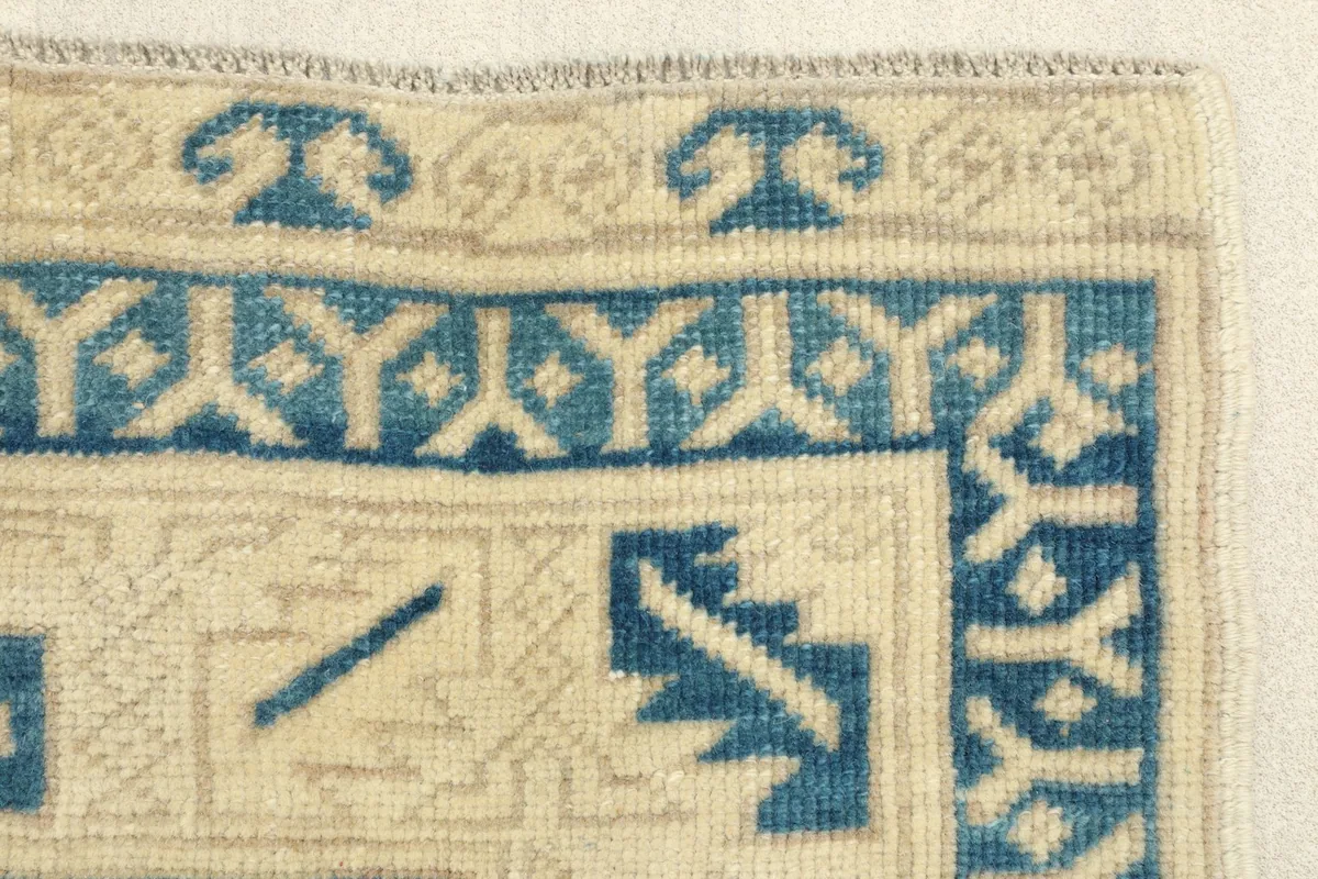 Close-up of the ivory and blue patterned border on the corner of the hand-knotted rug