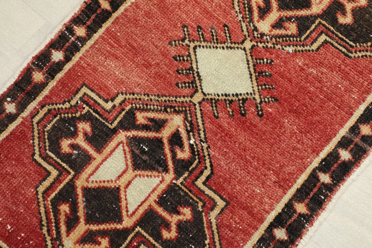 Angled view highlighting the red field and black and ivory geometric patterns of the rug.