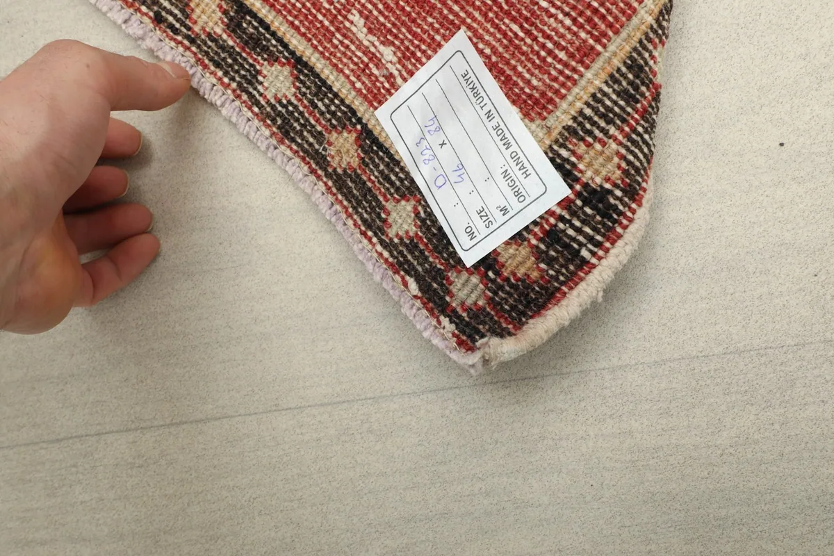 Hand pointing to the rug's fringe and a tag indicating its hand-knotted origin.