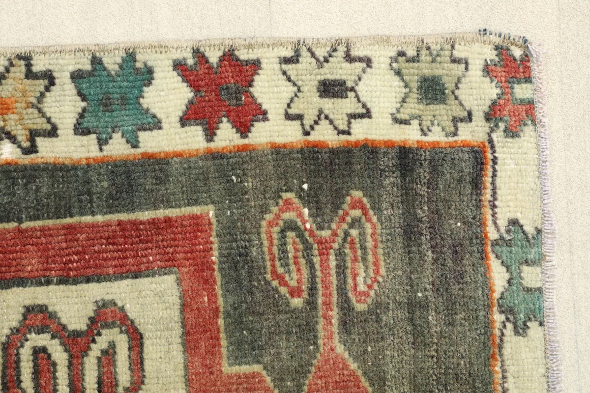 Close-up of the rug's edge, showing the charcoal field, red motifs, and cream border with patterned elements.