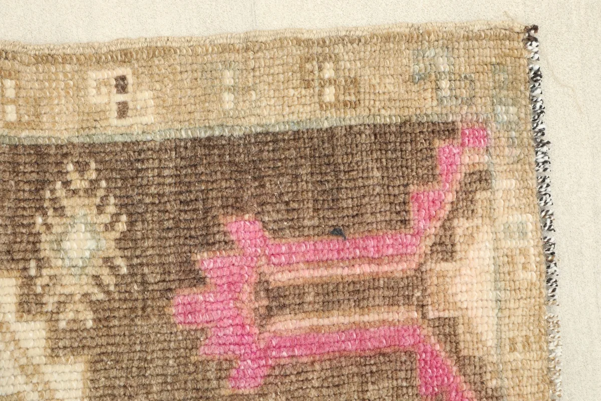 Close-up of a pink geometric element and the brown field, revealing the texture and slight wear.