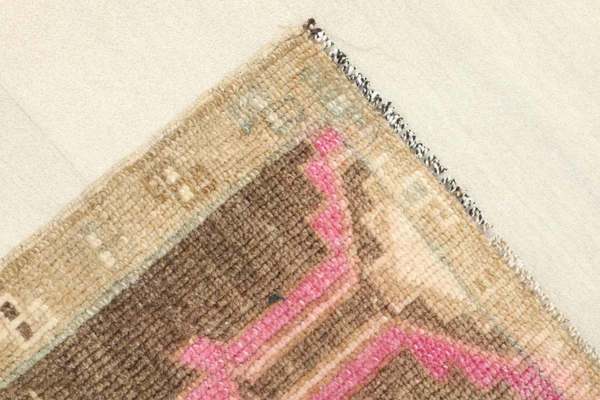 Corner detail showing the beige border and the subtle fringe of the hand-knotted wool rug.
