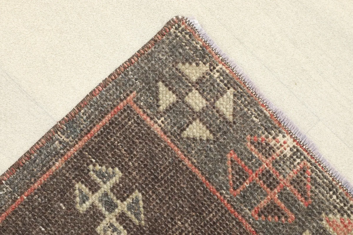 Corner detail of the rug, showing the charcoal border with beige and rust geometric elements.