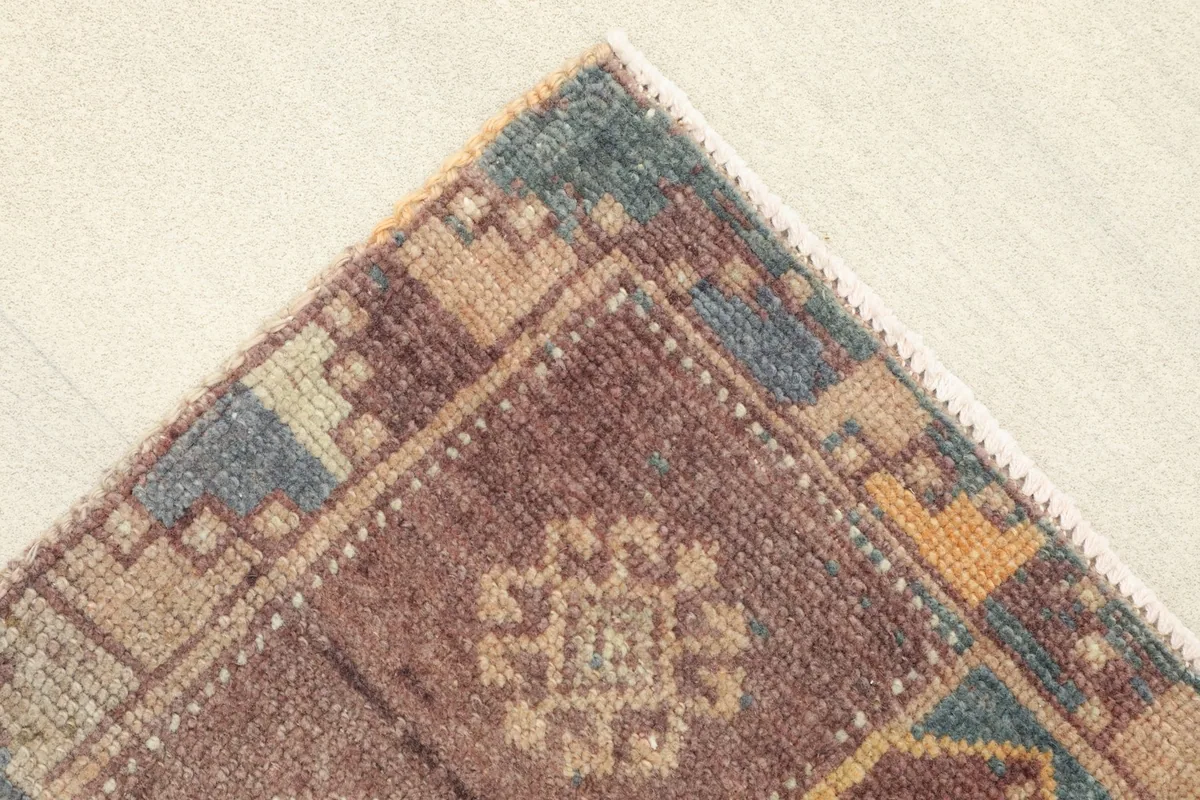 Corner detail showing the geometric border design in brown, blue, and gold, and the rug's construction.