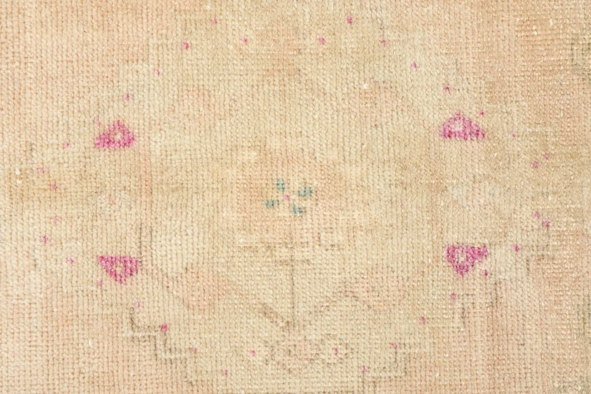 Close-up detail of the central tribal motif in rose and green on the beige field.
