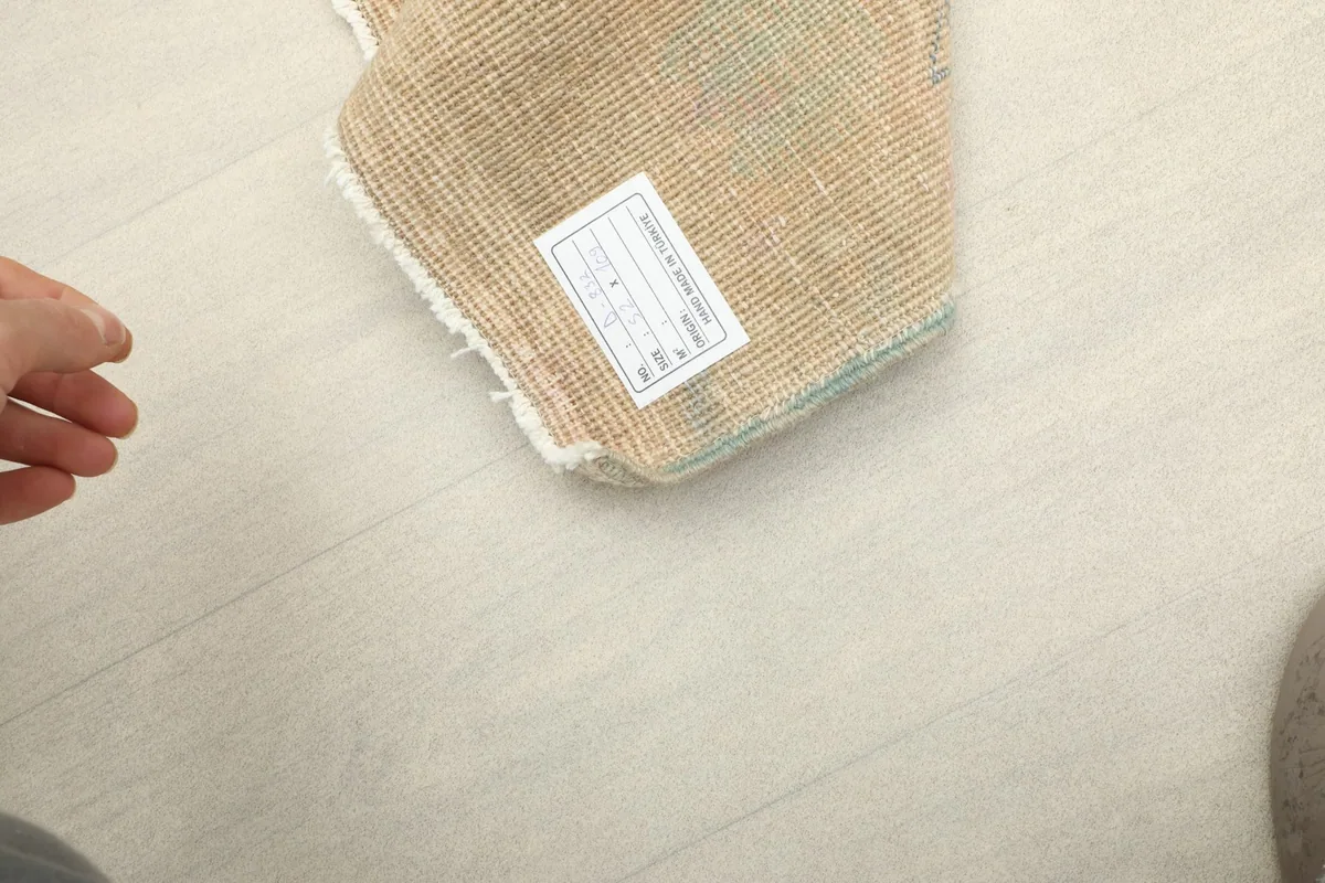 A hand pointing to the product label on the back of the vintage hand-knotted doormat.