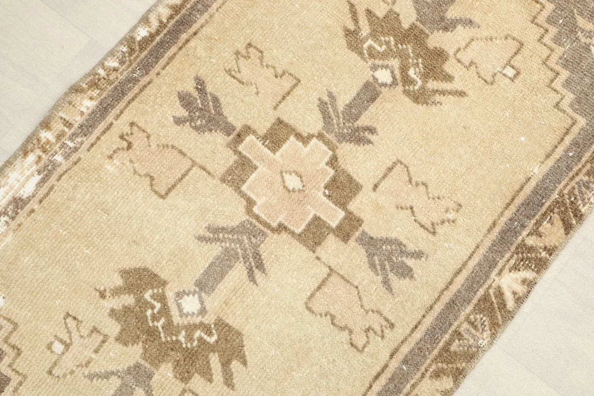 Angled view of the hand-knotted wool rug, highlighting the central geometric motif and distressed areas.