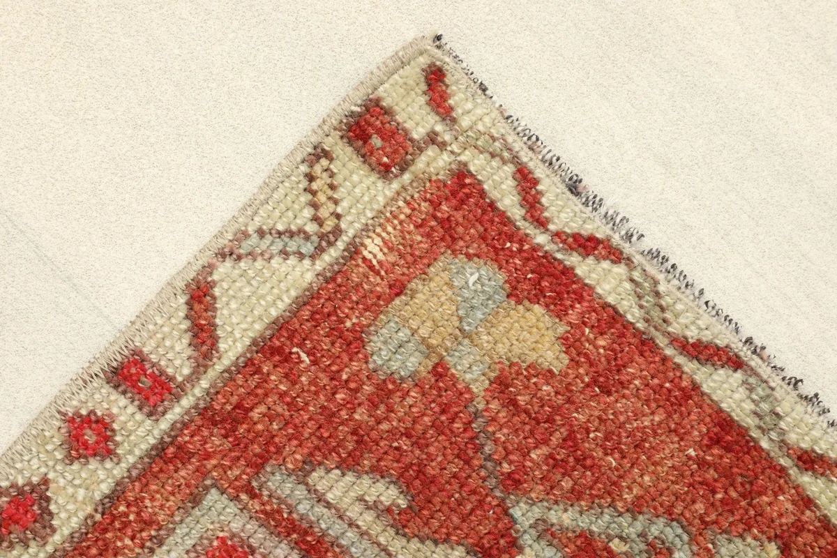 Corner detail of the rug, illustrating the beige border with small red and gray accents.