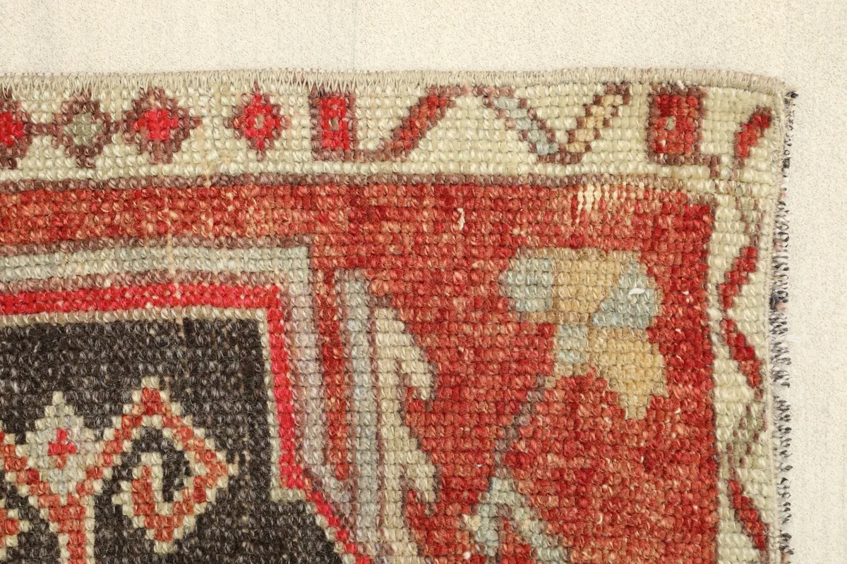 Edge detail of the rug, showing the transition from the red field to the beige and gray patterned border.