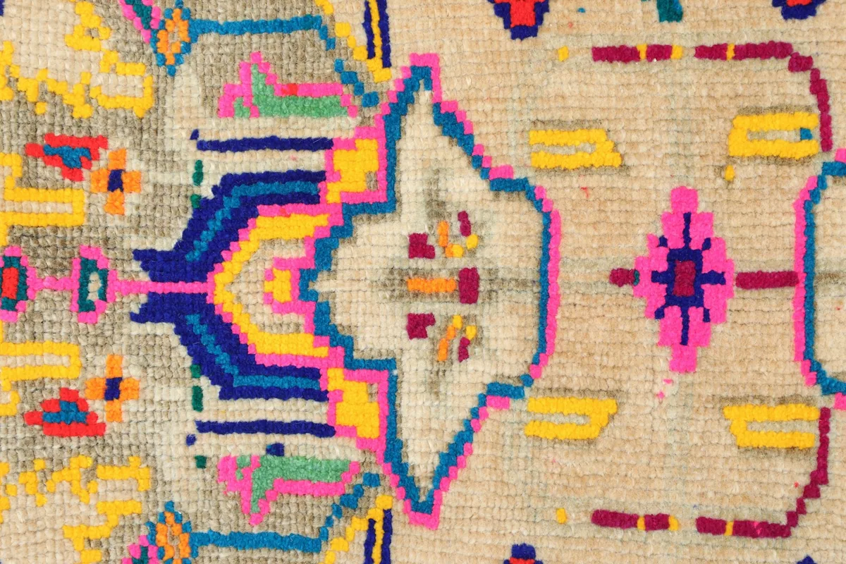 Close-up detail of the hand-knotted construction and the beige, pink, navy, yellow motifs.