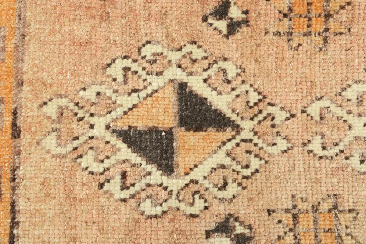 Detailed close-up of a prominent geometric diamond motif in black and ivory against the tan background.