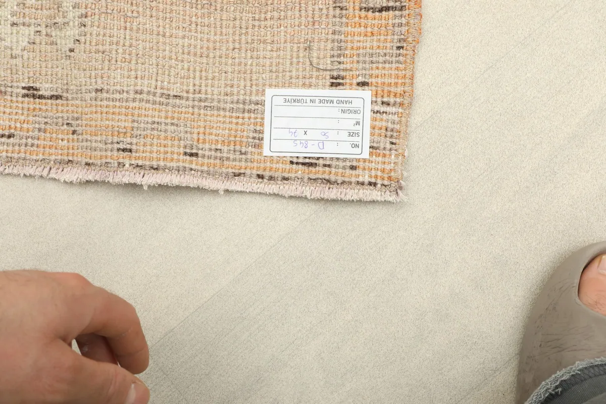 Close-up of the rug's reverse side, displaying the hand-knotted cotton foundation and a product label.