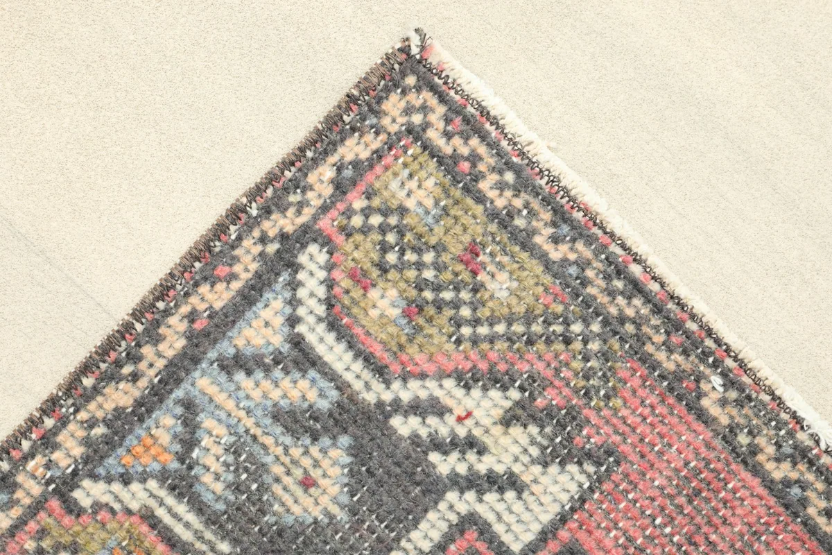 Corner detail showing the faded rose field, geometric motifs, and the woven border edge.
