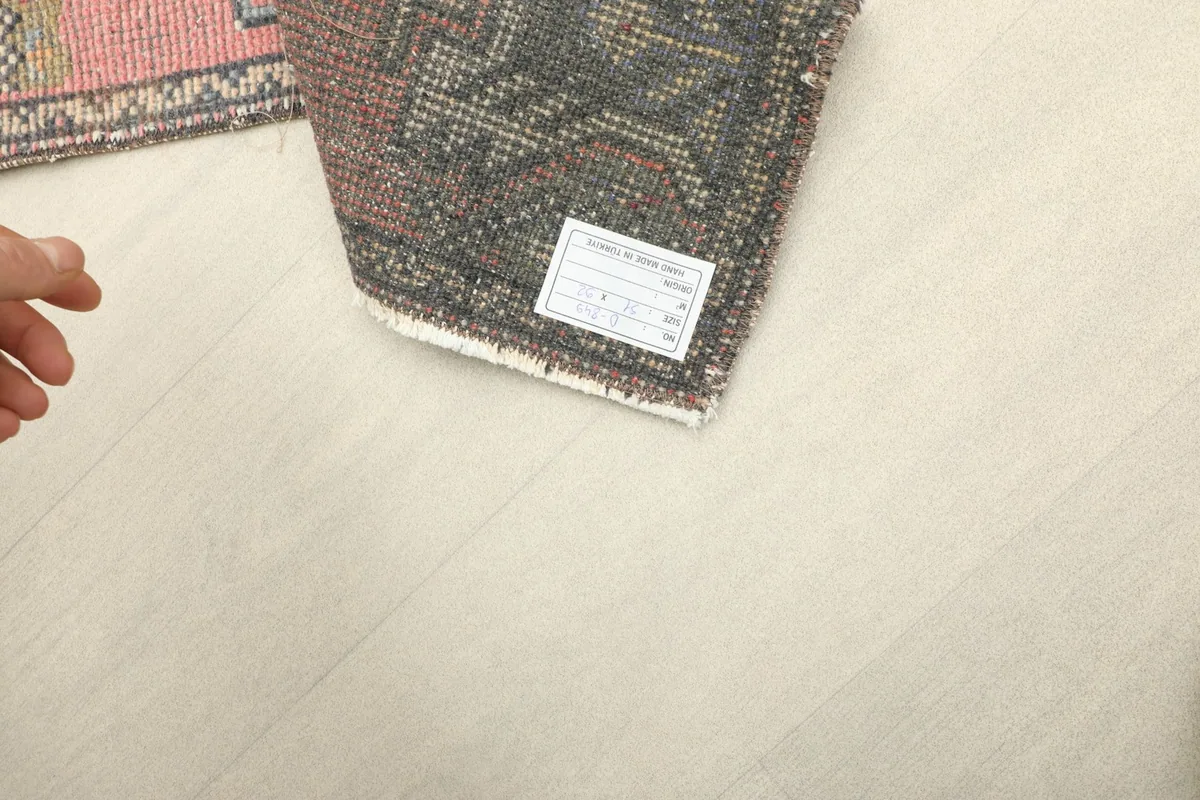Hand pointing to the label on the back of the vintage rug, showing the cotton foundation.