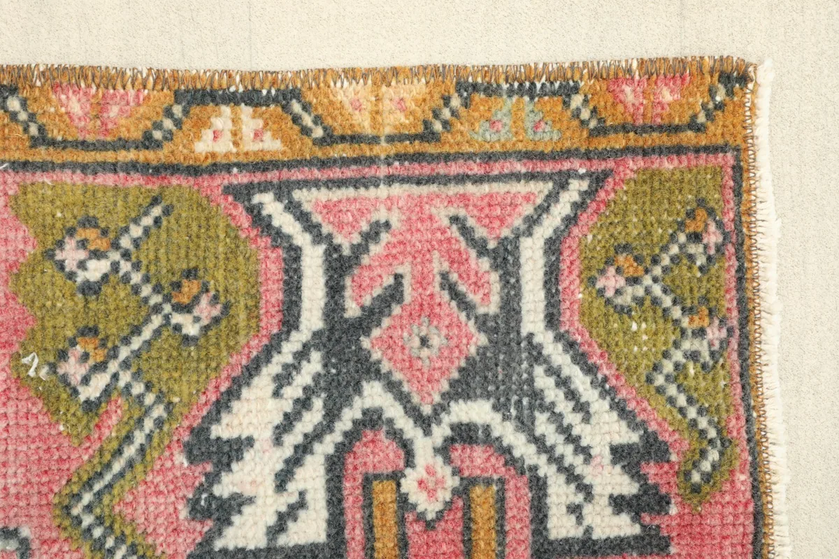 Close-up of the tribal motif in olive, black, and rose near the rug's edge.