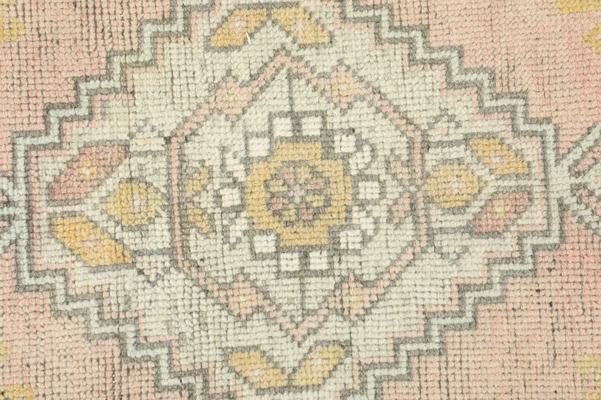 Detailed view of the central tribal motif with yellow and ivory accents on a pink field