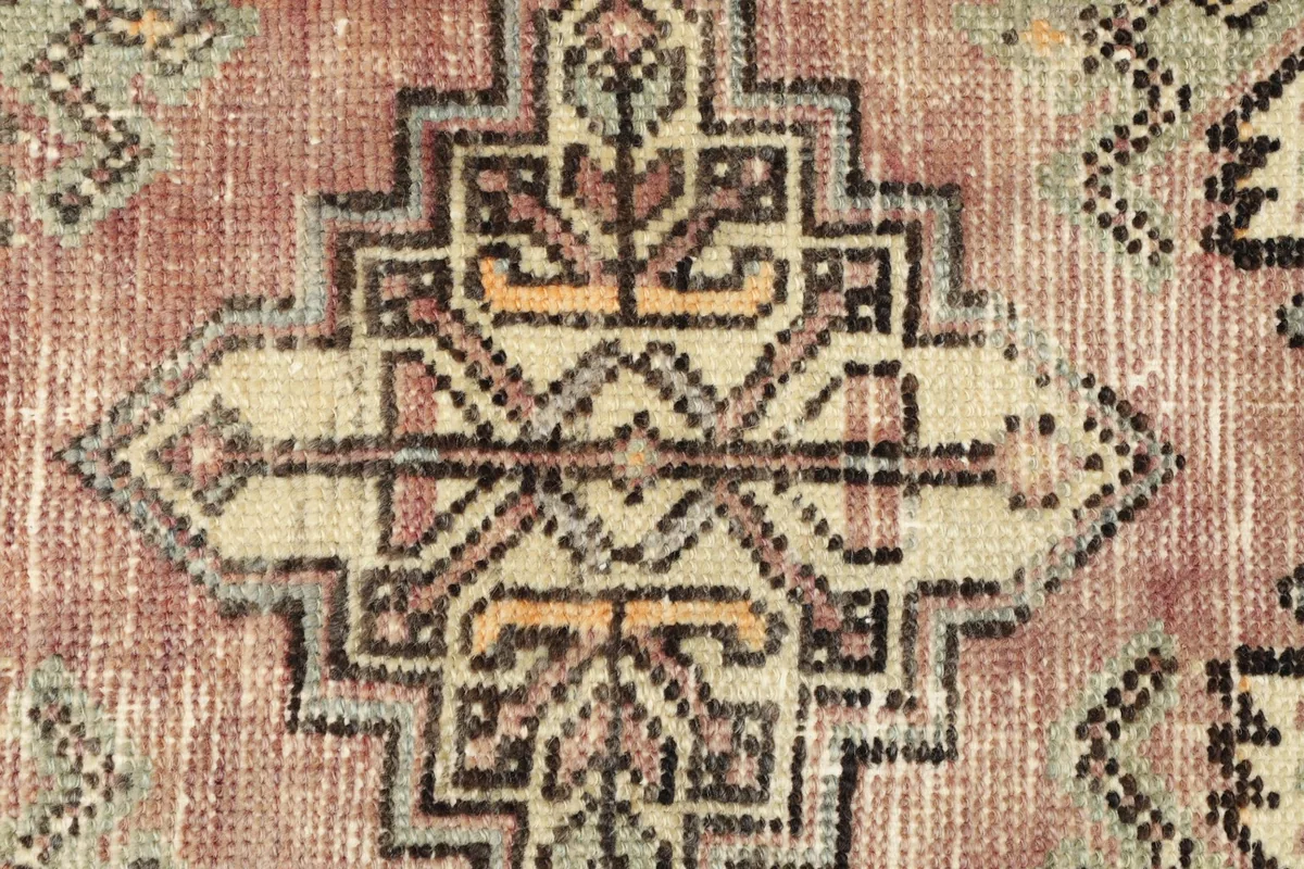 Close-up detail of the central ivory and gold geometric motif on the rose field.