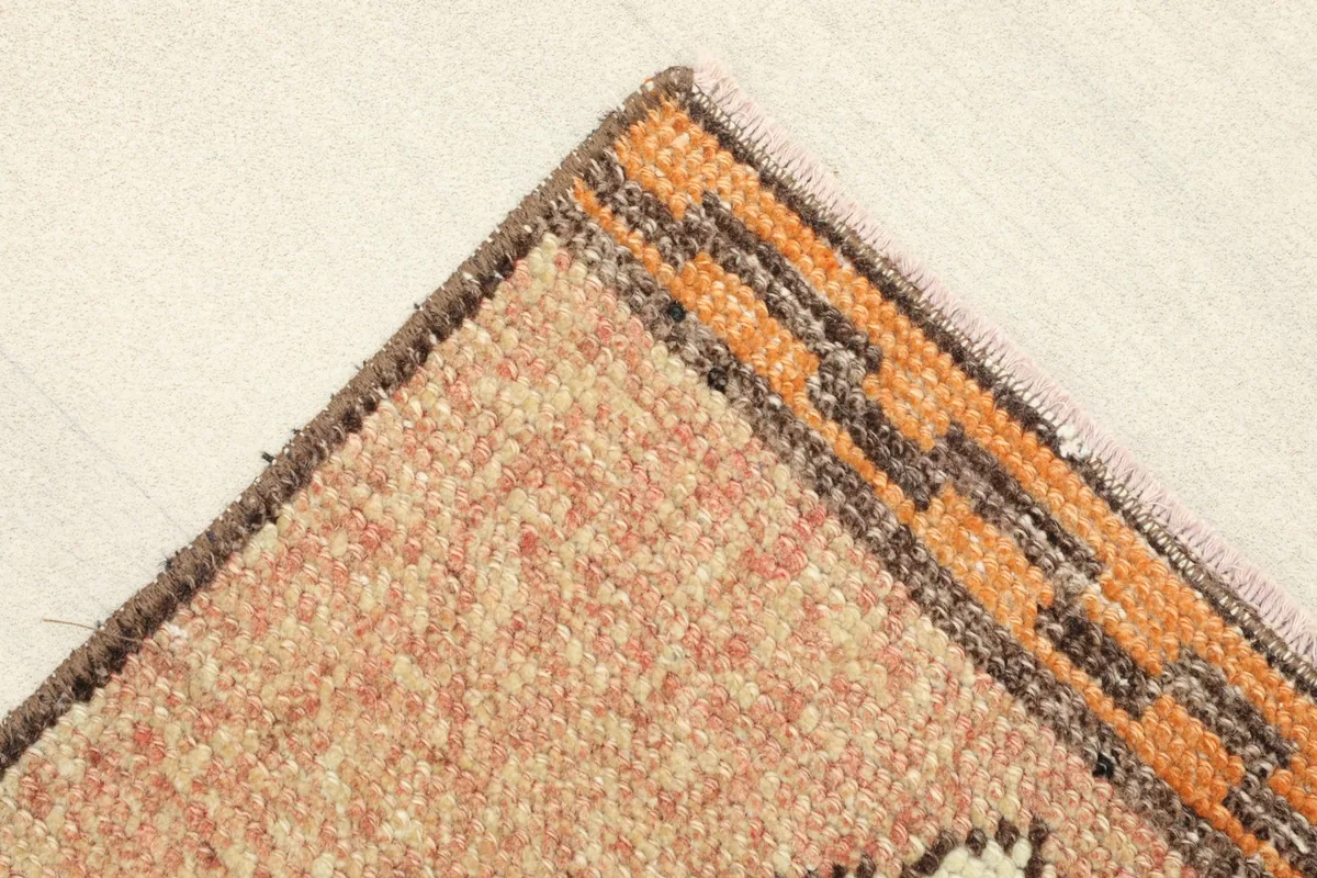 Corner view showing the orange and brown border design and the texture of the low wool pile