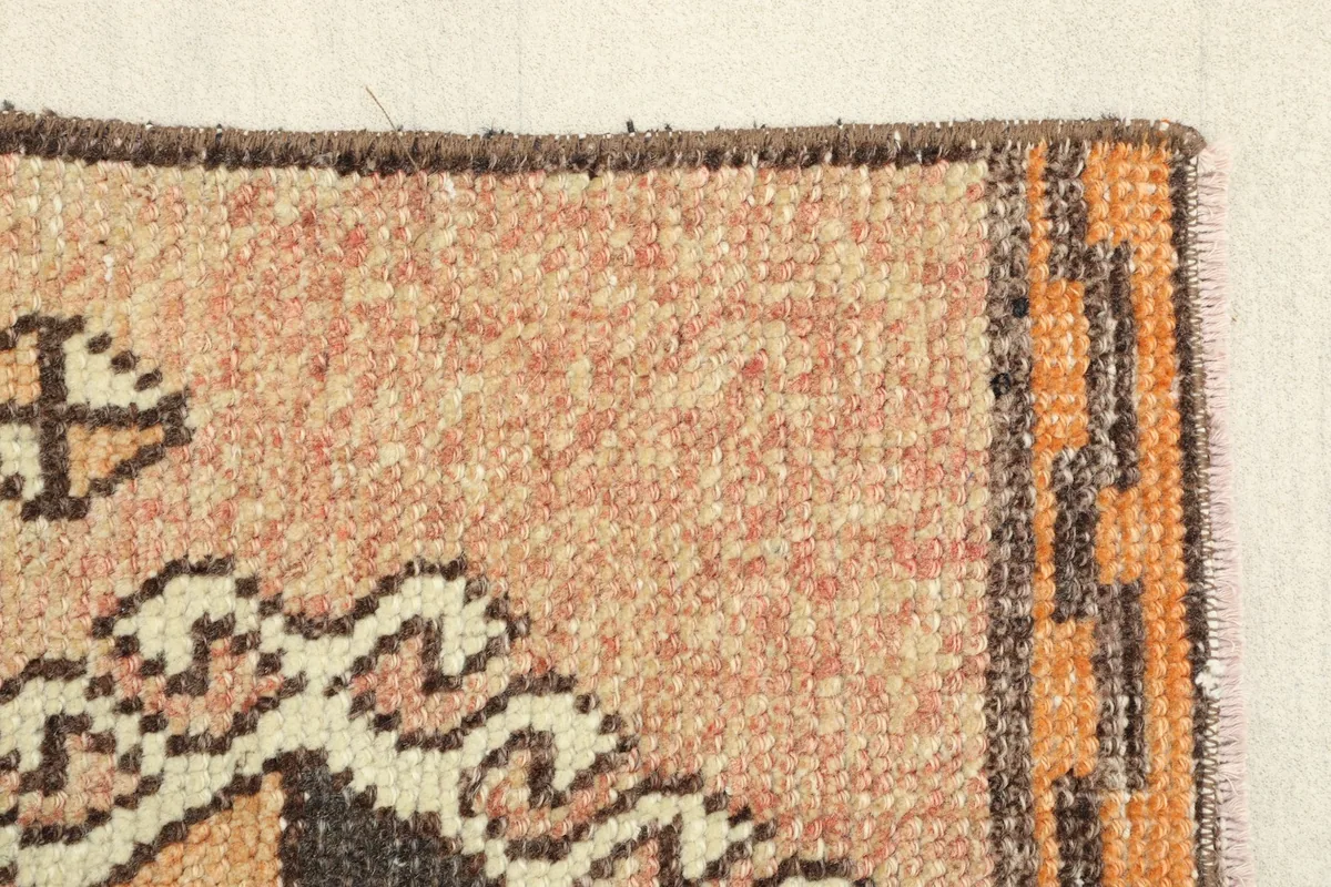 Side view of the rug's border, highlighting the transition from the tan field to the orange pattern
