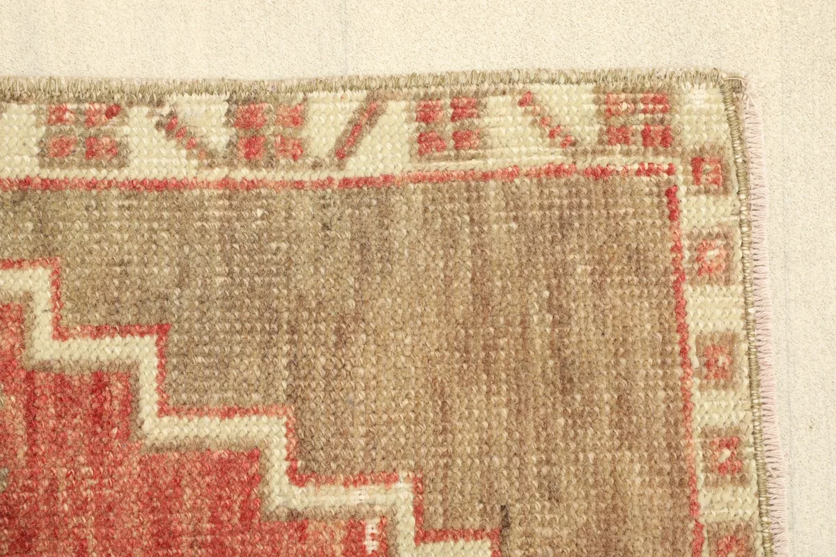 Close-up of a corner, displaying the geometric border patterns in cream and rust around the tan field.
