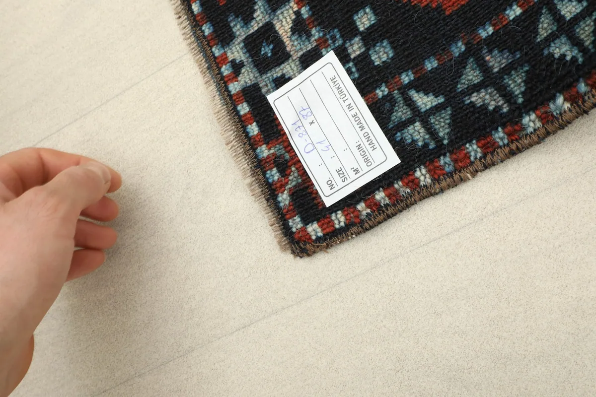 A hand next to the rug's label, indicating the small scale and craftsmanship
