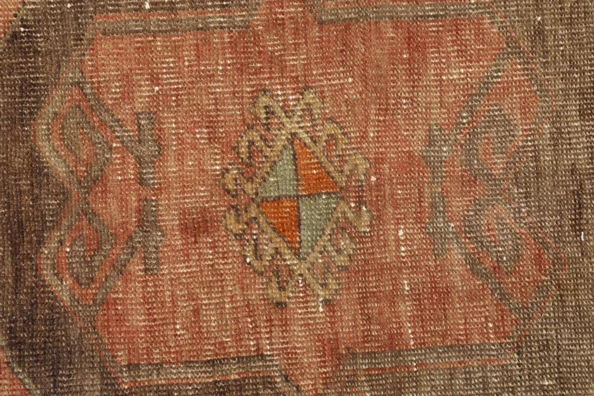Close-up detail of the rug's central geometric motif in brown, rust, and subtle green tones.