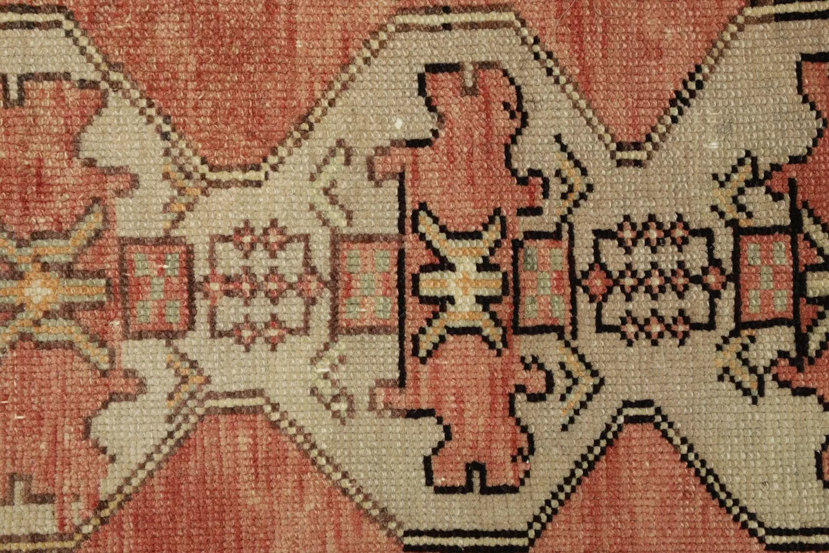 Close-up detail of the central geometric motifs in rose, beige, and black on the Anatolian rug.