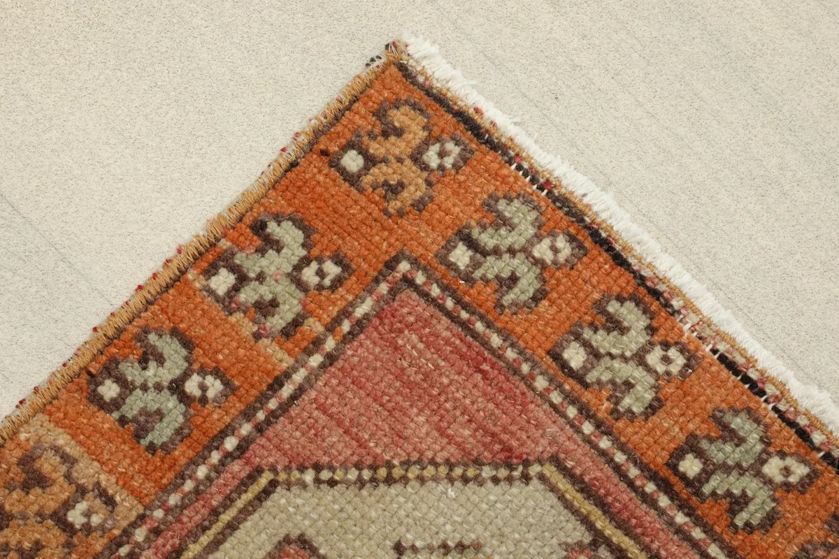 Corner detail showing the orange outer border with small geometric designs and the rug's edge.