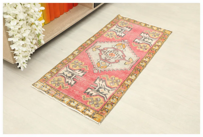 Full overhead view of the vintage rose and gold Anatolian doormat on a white floor next to a bookshelf.