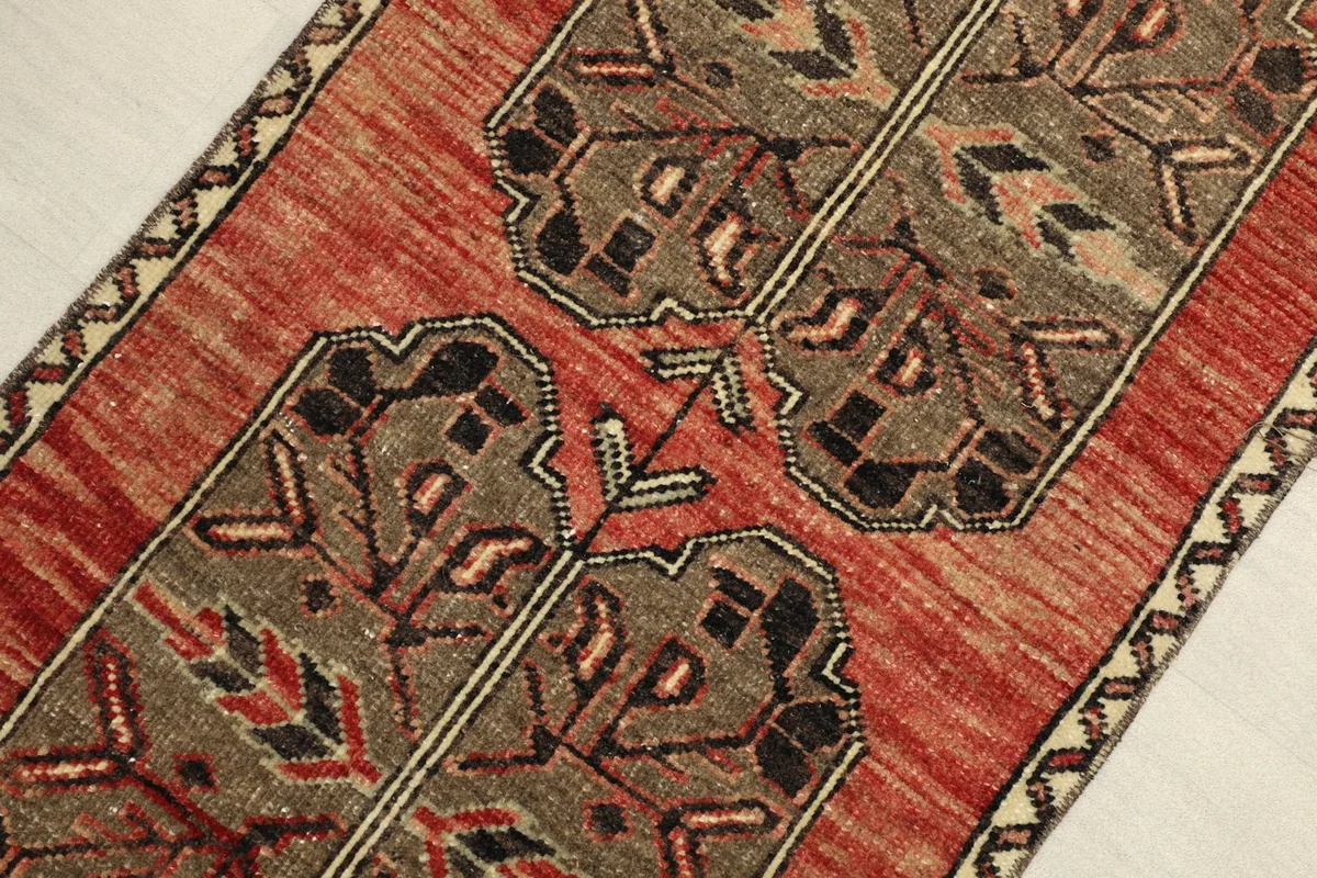 Angled view highlighting the texture of the low wool pile and the intricate geometric designs in red, brown, and black.