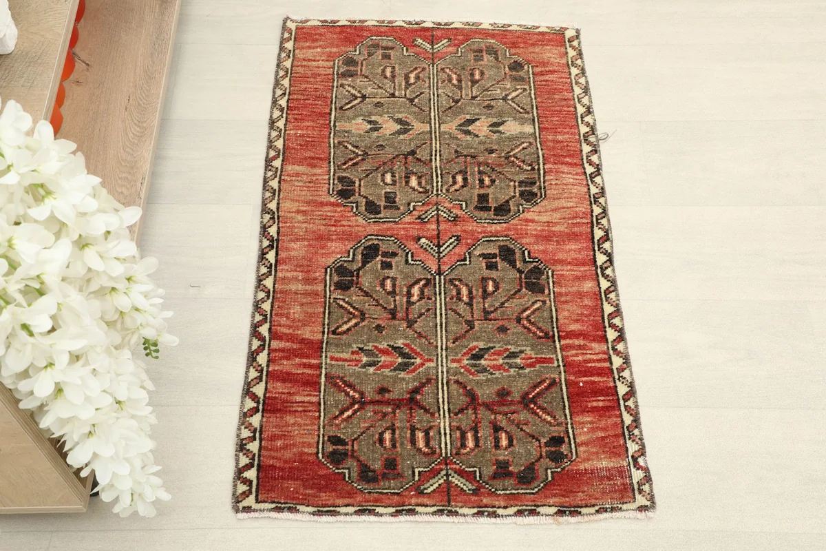 Overhead view showcasing the red field and central brown and black tribal geometric patterns of the small rug.