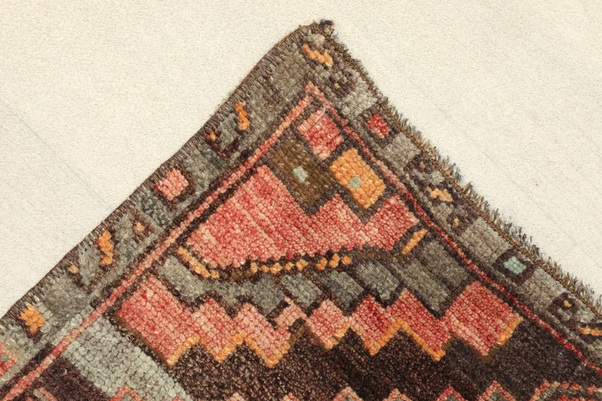Corner detail showing the geometric border design and the frayed edges of the vintage doormat.