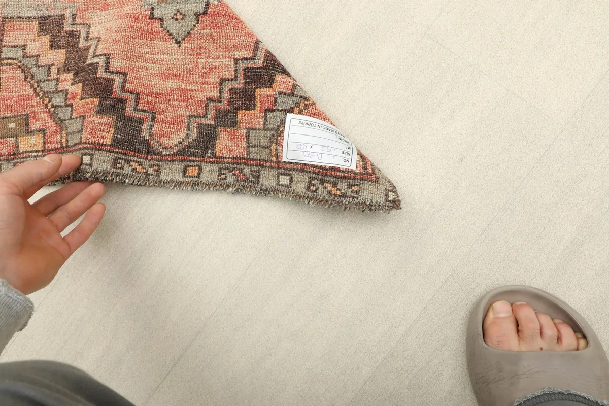 A hand holding up a corner of the rug, displaying the back of the hand-knotted wool pile on cotton foundation.