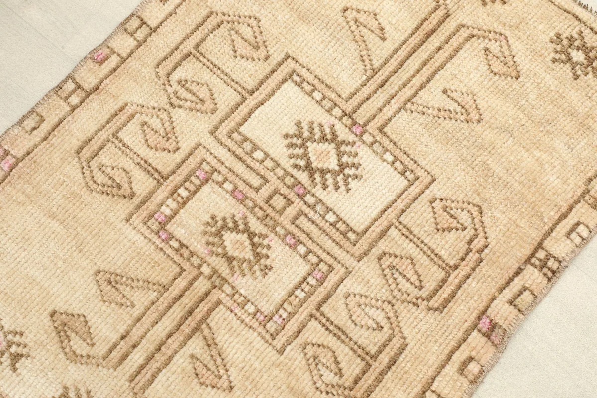 Angled close-up of the rug's beige field and central brown geometric motifs with pink details.