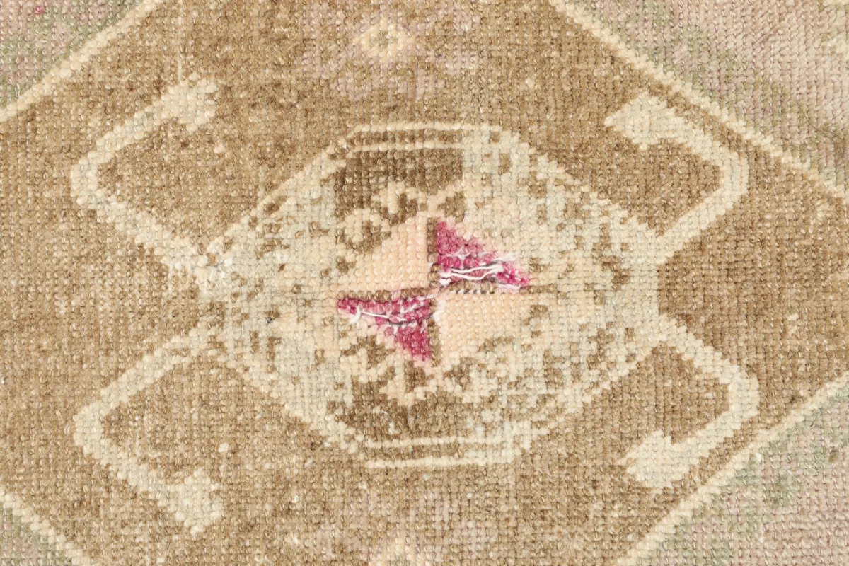 Tight detail shot focusing on the intricate knotting and the muted pink and beige colors in the main motif.