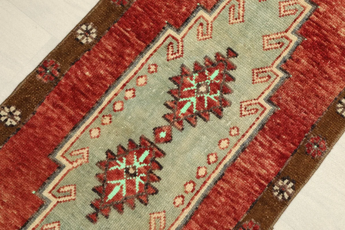 Angled close-up of the rug's central green medallion and the surrounding rust field, showing knot detail.