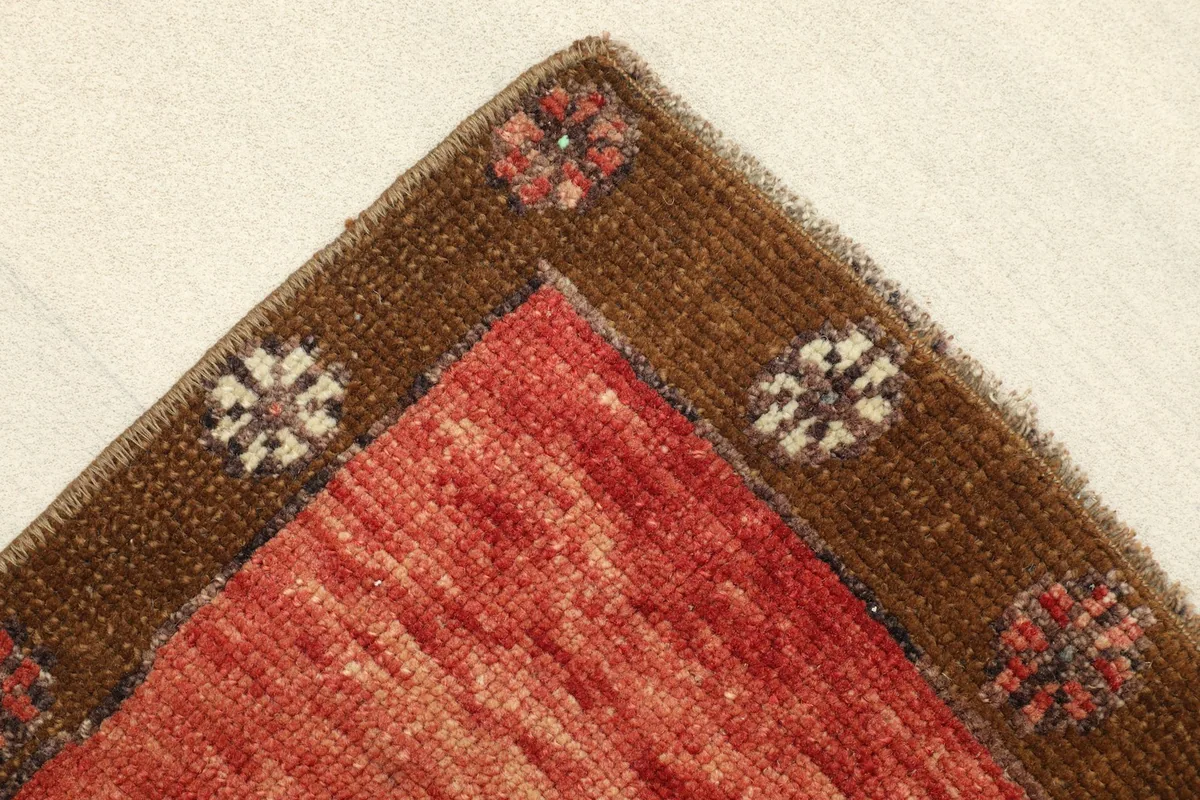 Close-up of the corner, showing the brown border with floral-like motifs and the texture of the wool pile.