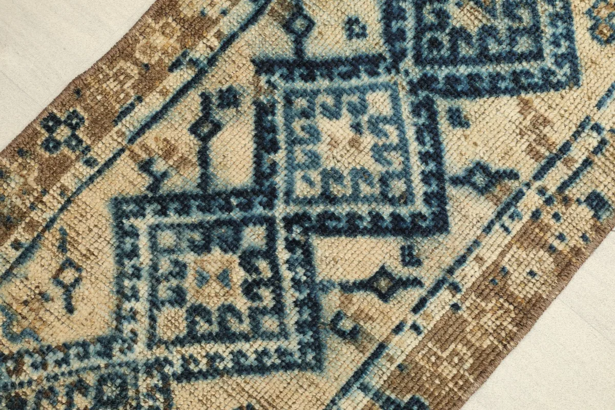 Angled close-up of the rug's surface, highlighting the navy and beige geometric motifs and brown border.