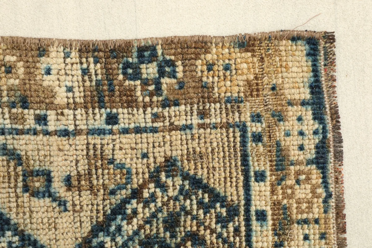 Detail of the rug's brown border and a section of the beige field with subtle patterning.