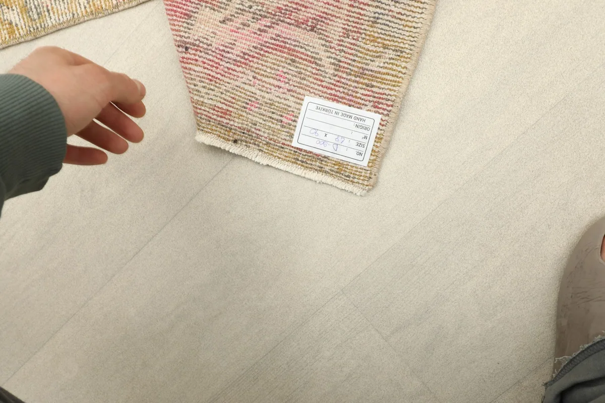 Hand next to the rug showing its actual size and the tag indicating origin and material