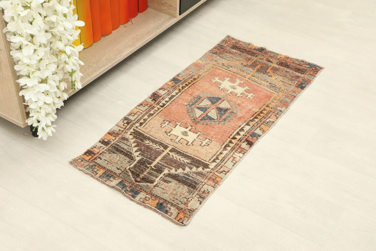 Overhead view of the small rug placed on a light floor next to a white and wood cabinet.